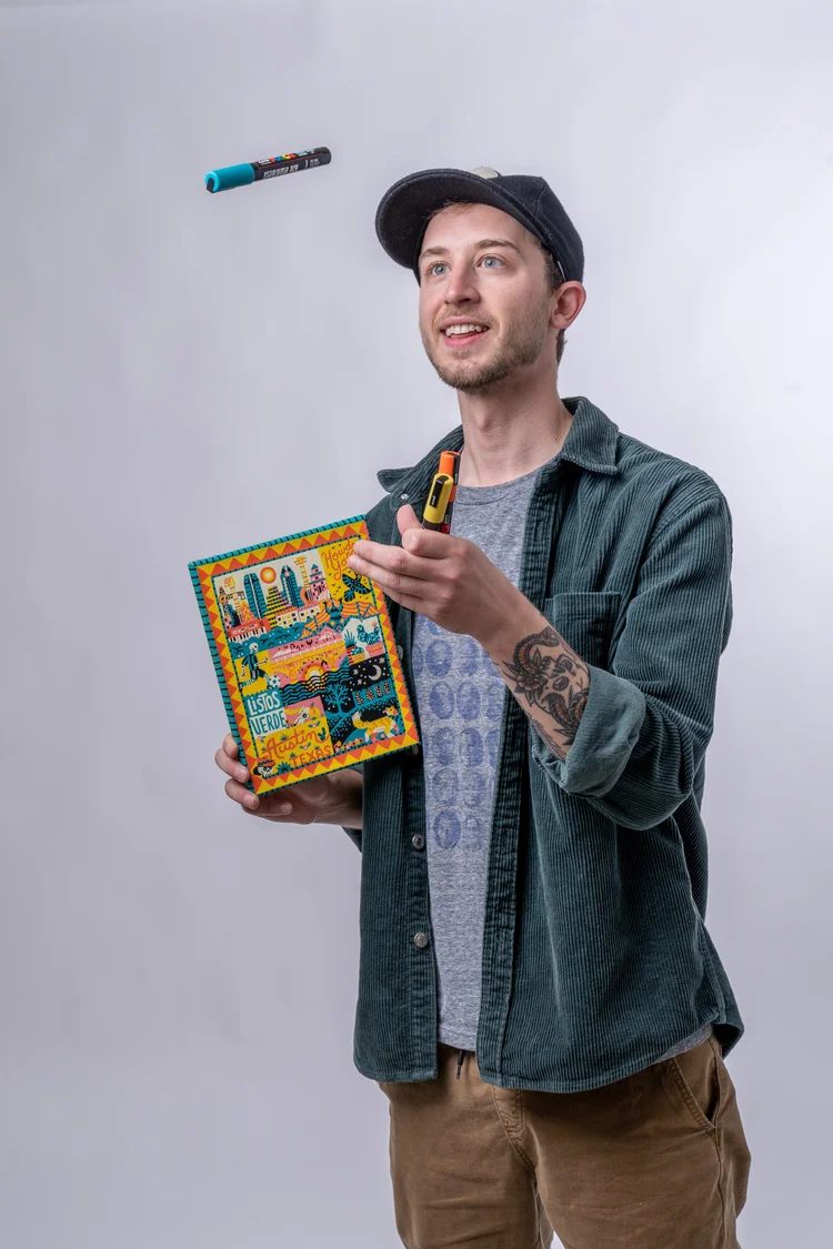A man in a cap holds a colorful book and a marker, with a floating marker above his head.