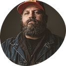 Man wearing a red cap and denim jacket against a dark background.
